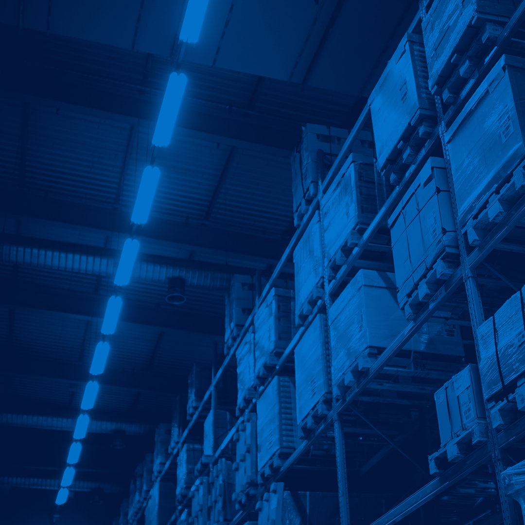 Warehouse interior with tall metal shelving racks stacked with pallets and boxes, tinted in a blue colour overlay.