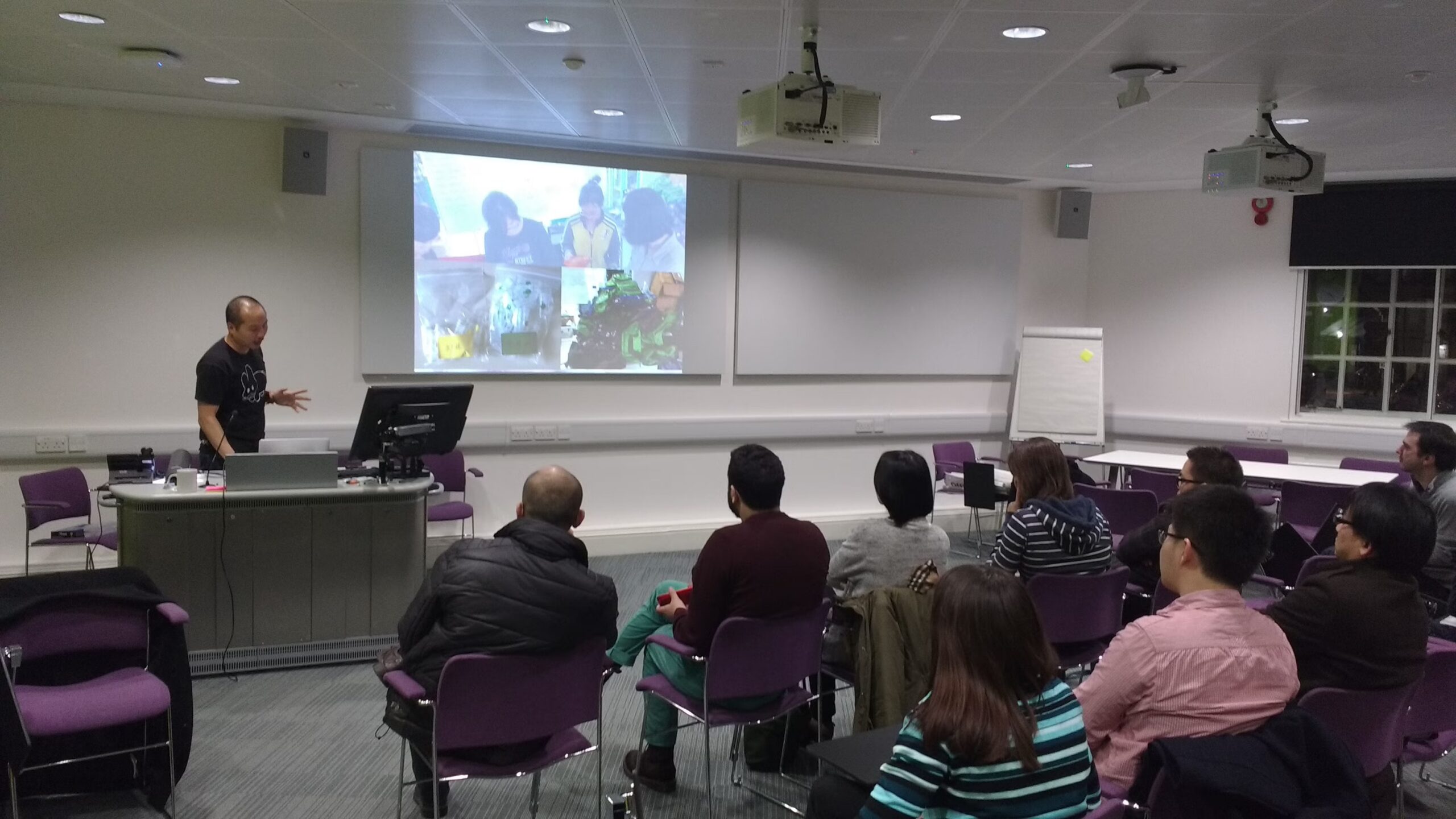 Audience attending a technical talk in a lecture room with a speaker presenting slides at the front